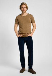 Maglietta corta in cotone marrone con collo rotondo, abbinata a pantaloni aderenti blu scuro e stivali alla caviglia marroni. Design semplice e testurizzato.