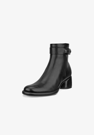 Bottine en cuir noir avec un bout arrondi, un large talon carré et une sangle avec une boucle en métal argenté autour de la cheville. Texture lisse.