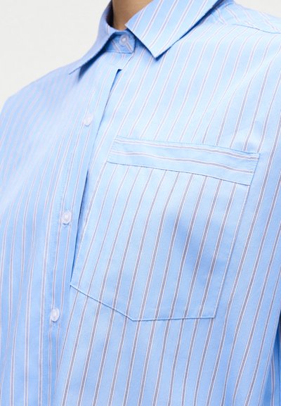 Ανοιχτό μπλε πουκάμισο με κάθετες λευκές και ροζ ρίγες και τσέπη στο στήθος με οριζόντια ριγέ περιθώριο.