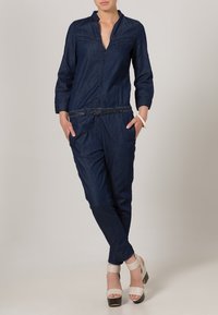 Marinblå denimoverall med krage, långa ärmar och cinchad midja. Har framfickor och en lätt bältesdetalj. Chunky klackar.