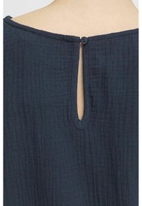 Mörkblått tyg med en texturerad yta. Baksidan har en liten nyckelhålöppning som säkras med en enda svart knapp.