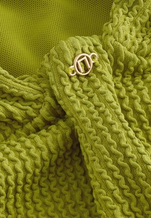 Tissu tricoté vert avec une texture côtelée et un détail de boucle circulaire dorée. Design doux et flexible avec un motif ondulé continu.