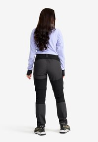 Sittande svarta vandringsbyxor med grå paneler, elastisk midja och fotledsdetaljer. Matchas med en ljuslila långärmad topp.