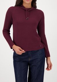 Geribbelde, pruimkleurige top met een col en trekkoorddetails. Lange mouwen en een ontspannen pasvorm. Gecombineerd met donkerblauwe denim.