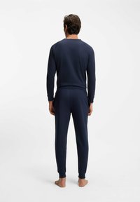 Laivastonsininen oloasusetti, joka sisältää pitkähihaisen yläosan ja kapealahkeiset housut, valmistettu pehmeästä kankaasta, jossa on resorit hihansuissa ja vyötärössä.