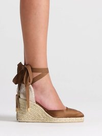 Jambe portant une espadrille compensée en satin marron avec une semelle en jute tressée et un lien à nouer autour de la cheville sur un fond neutre.