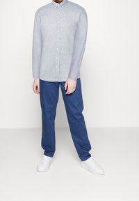 Jasnoniebieska koszula na guziki z długim rękawem, zestawiona z granatowymi spodniami i białymi tenisówkami. Prosty design i przewiewna tkanina.