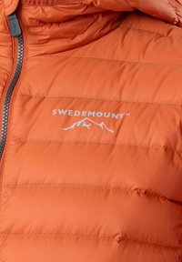 Oranje gewatteerde jas met een gestikte uitstraling, voorzien van een voorrits en het "SWEDEMOUNT" logo met een berggraphic in het wit.