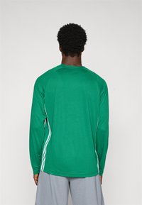 Grøn langærmet træningsskjorte med en struktureret stof, der har hvide sidelister og en rund halsudskæring, parret med grå shorts.