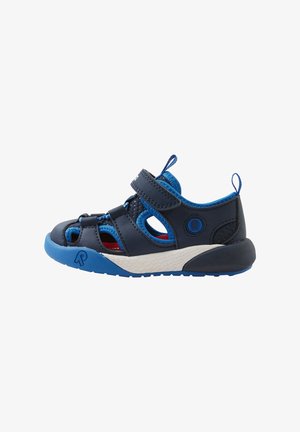 Sandal azul marinho com detalhes azuis, apresentando um design recortado, tiras de velcro, sola texturizada e forro interior vermelho. Sola de borracha para aderência.