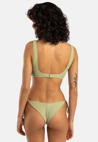 Bikini verde chiaro a coste con top a spalline larghe e parte inferiore con fiocco ai lati, caratterizzato da un design con schiena bassa e accenti hardware minimi.
