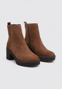 Bottes ankle en suède marron avec un talon épais empilé, une fermeture éclair latérale et une semelle texturée. Surface lisse avec des détails de couture subtils.