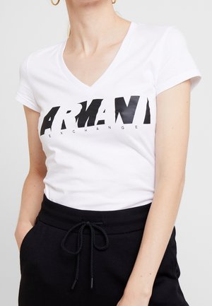T-shirt blanc à manches courtes avec col en V, arborant un logo graphique noir "ARMANI EXCHANGE" sur la poitrine, confectionné en coton doux.