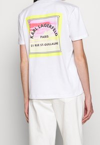 Biała bawełniana koszulka z kolorowym wzorem graficznym na plecach, z tekstem, w tym "KARL LAGERFELD" i "21 RUE ST-GUILLAUME."