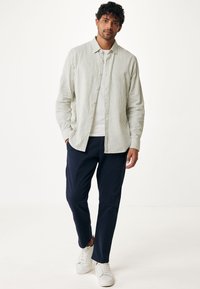 Světle zelená a bílá pruhovaná košile na knoflíky, nošená přes bílý tričko, v kombinaci s námořnickými kalhotami a bílými teniskami. Klasický ležérní styl.