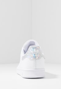 Vita lädersneakers med en slät yta, med en holografisk hälflik. Designen inkluderar perforeringar och en solid gummisula.