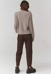 Jasnoszary, teksturowany sweter o luźnym kroju, w zestawieniu z brązowymi, tapered spodniami i czarnymi butami z masywną podeszwą.