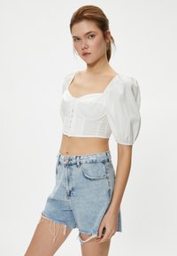 Weißes Cropped Top mit Puffärmeln und strukturiertem Muster, kombiniert mit hochgeschnittenen, verwaschenen blauen Jeansshorts.