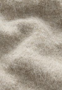 Beige wollen stof met een zachte textuur, voorzien van een fijn gebreid patroon en delicate pluisjes, met subtiele kleurvariaties.