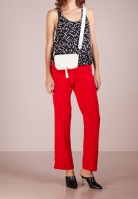 Černý bezrukávový top s bílými puntíky, červené široké kalhoty a malá bílá crossbody kabelka. Celý outfit doplňují černé špičaté muly.