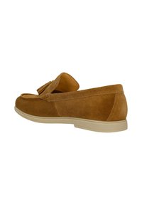 Mocassin en daim marron avec pompons, semelle beige et petit talon, présenté de profil sur fond blanc.