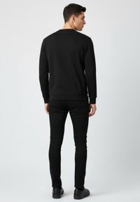 Sudadera negra con mangas largas y cuello redondo, combinada con pantalones negros de corte ajustado. La tela parece lisa con detalles mínimos de costura.