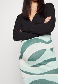 Pletené šaty s černým žebrovaným topem a sukní s vlnitým vzorem v zeleno-bílé barvě, se zvýrazněním obepínajícího tvaru a strukturovaného materiálu.