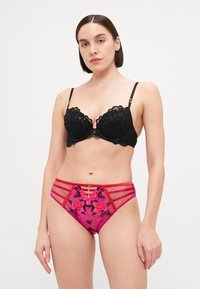 Black lace bra with scalloped edges and floral embroidery. High-waisted pink panties featuring black floral patterns and decorative straps.