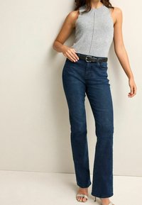 Gray sleeveless top with a high neckline, paired with dark denim flared jeans. Includes a black belt with silver hardware.