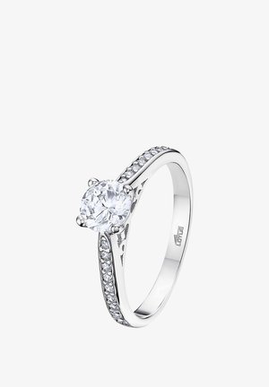 Silver ring featuring a large round cubic zirconia at center, flanked by smaller stones along the band; smooth, polished finish.