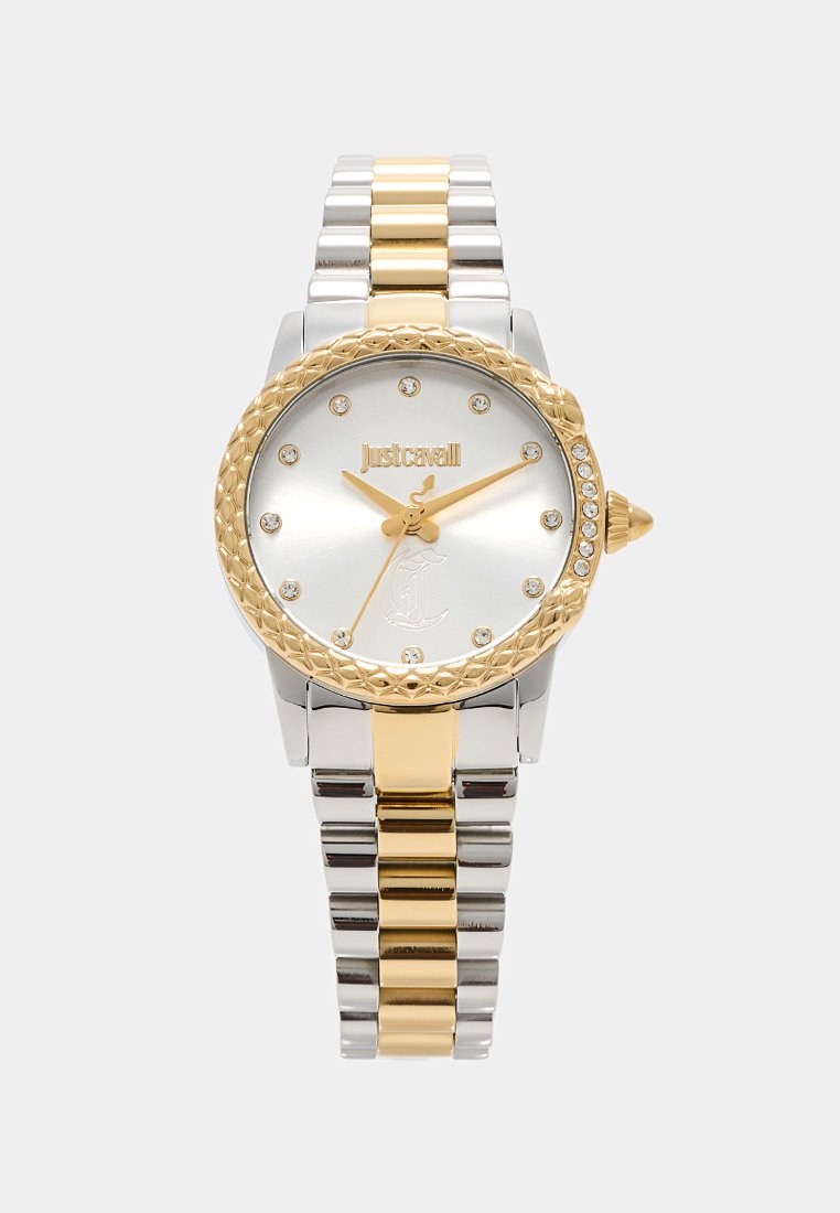 Montre-bracelet en métal doré et argenté avec une lunette texturée, un cadran argenté, une forme arrondie et ornée de pierres transparentes. Nom de la marque affiché.