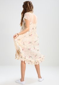 Krémové midi šaty s květinovým vzorem, volánkovým lemem, průhlednými rukávy a upnutým korzetem. Vyznačují se jemným růžovým vzorem a lehkým materiálem.