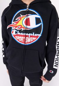 Felpa con zip nera realizzata in misto cotone. Presenta un grande logo multicolore sul petto, tasca a marsupio e branding lungo le maniche.