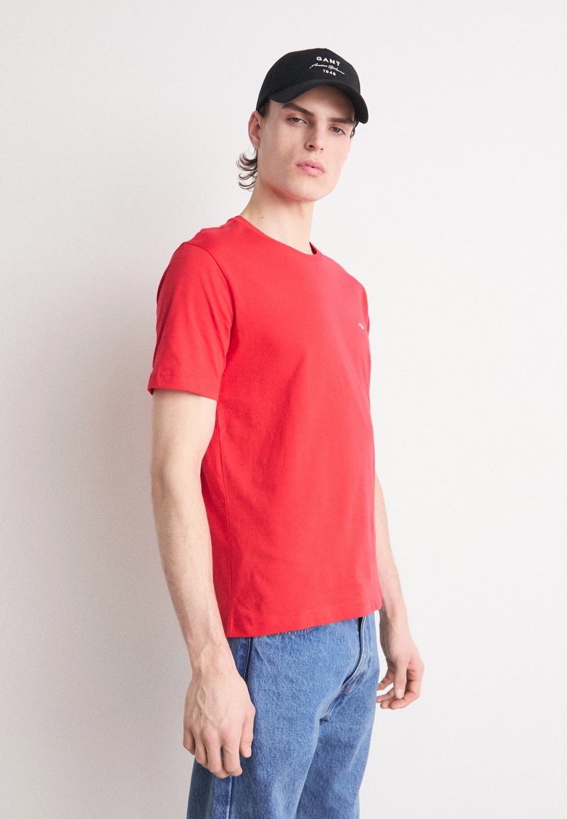 T-shirt en coton rouge avec un col rond, des manches courtes et un petit logo sur la poitrine. Associé à un jean en denim bleu clair.