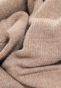 Tessuto a maglia beige, morbido al tatto con cuciture visibili, che presenta un aspetto accogliente e caldo in una disposizione spiegazzata e piegata.