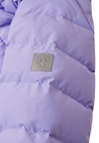 Violeta pūkaina jaka ar quilted dizainu, kurai ir pelēks taisnstūra logotipa uzlīme un gluda, spīdīga auduma tekstūra.