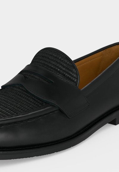 Juoda odinė loafer batai su tekstūruotu austiniu viršumi, penny dirželio detalė ir rusvos odos vidinis pamušalas ant balto fono.