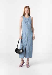 Lys blå denim maxikjole med frontknaplukning, sideslids, parret med en sort skuldertaske og lilla hæl sandaler.