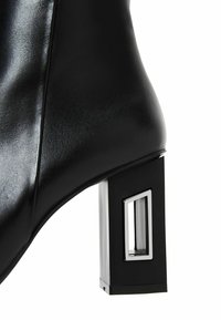Zwarte leren enkellaars met een geometrische blokhak met een transparante inset en glanzende metalen accenten. Glad textuur en gestructureerd ontwerp.