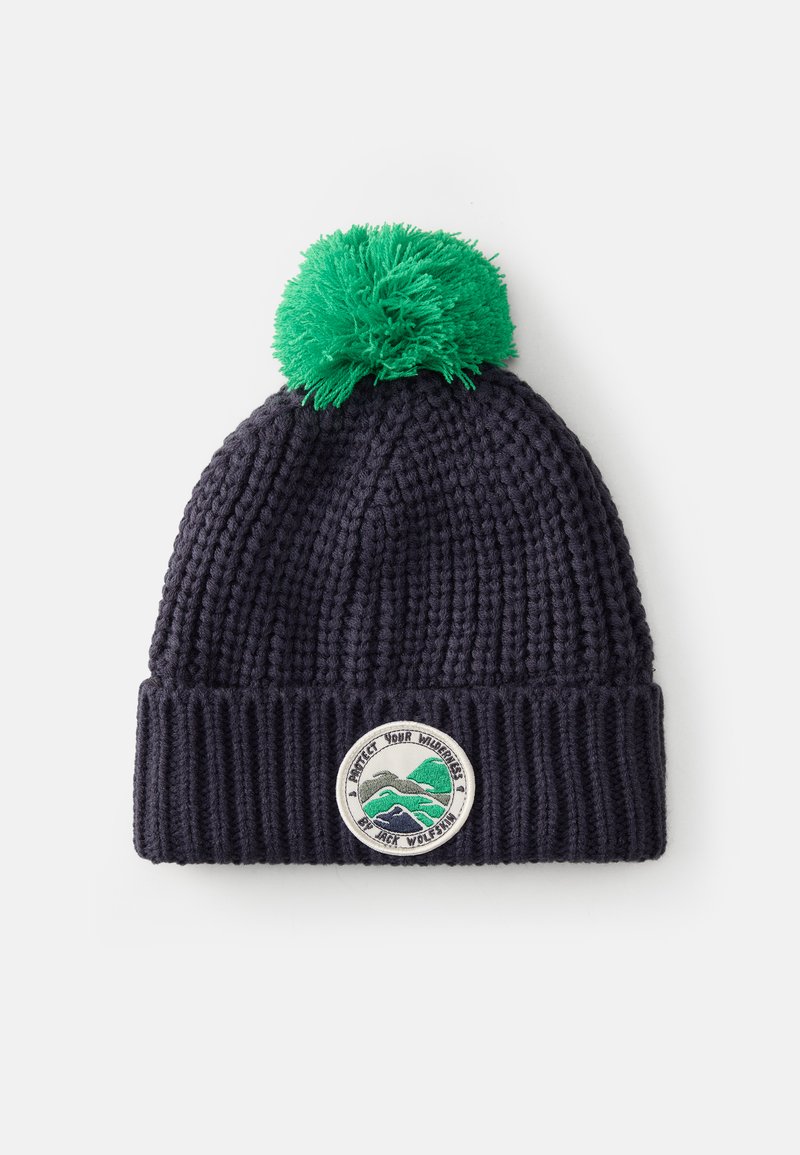 Berretto lavorato a maglia di colore blu navy con un pom-pom verde e una toppa circolare con montagne e la scritta "Proteggi la tua natura selvaggia". Design tessuto.