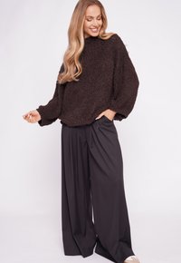 Brown textured sweater with oversized fit and ribbed cuffs, paired with loose black wide-leg trousers. Simple, neutral color palette.