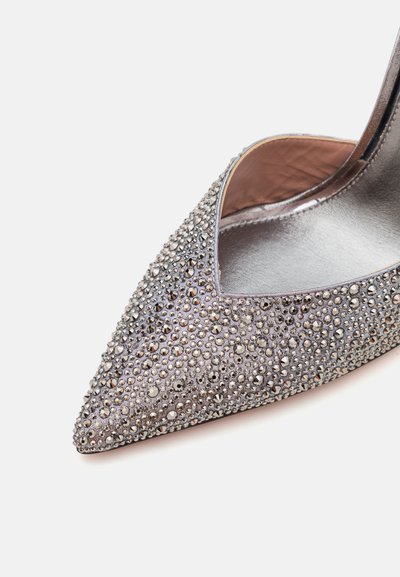 Zapato de tacón alto plateado con punta afilada, que presenta una textura de cuentas y adornos brillantes en la parte superior.