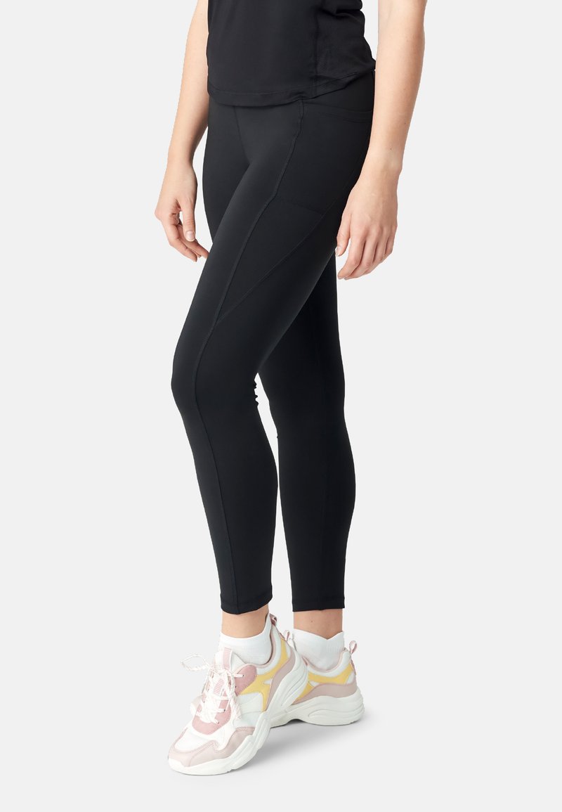 Leggings neri con una vestibilità affusolata, caratterizzati da cuciture a contrasto e una texture liscia. Abbinati a scarpe da ginnastica bianche e in tonalità pastello.