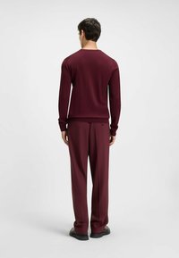 Bordeauxfarbener Pullover und Hose, leichtes Strickmaterial, enganliegende Manschetten und lockerer, gerader Schnitt. Glatte Textur und subtile Glanz.