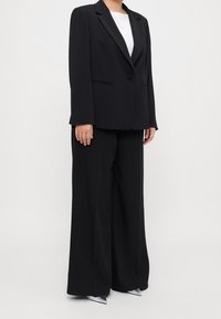 Czarny, dopasowany garnitur z jednorzędową marynarką o klapach z wcięciem oraz szerokimi spodniami. Gładka tkanina o eleganckim wykończeniu.