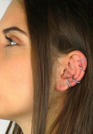 Silberne Creolen schmücken das obere Ohr, mit gedrehten Designs und einer glatten Oberfläche, hervorgehoben vor mittelbraunem Haar.