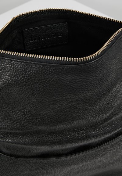 Interno di una borsa in pelle nera con una finitura testurizzata, cerniera dorata e un'etichetta di marca visibile all'interno.