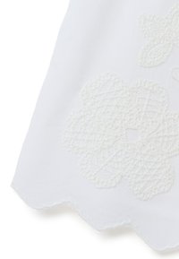 Tessuto bianco con ricami floreali texturizzati. Presenta bordi scallop e cuciture intricate in un sottile motivo in rilievo.