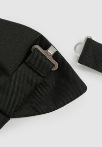 Svart texturerad tyg med en slät lyster, med en metallklämma och ett band. Designen inkluderar en rosett och diagonala ribbor.