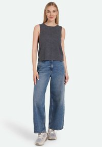 Gray sleeveless top paired with loose-fitting light blue denim jeans. Model stands in casual sneakers, showcasing a relaxed outfit.